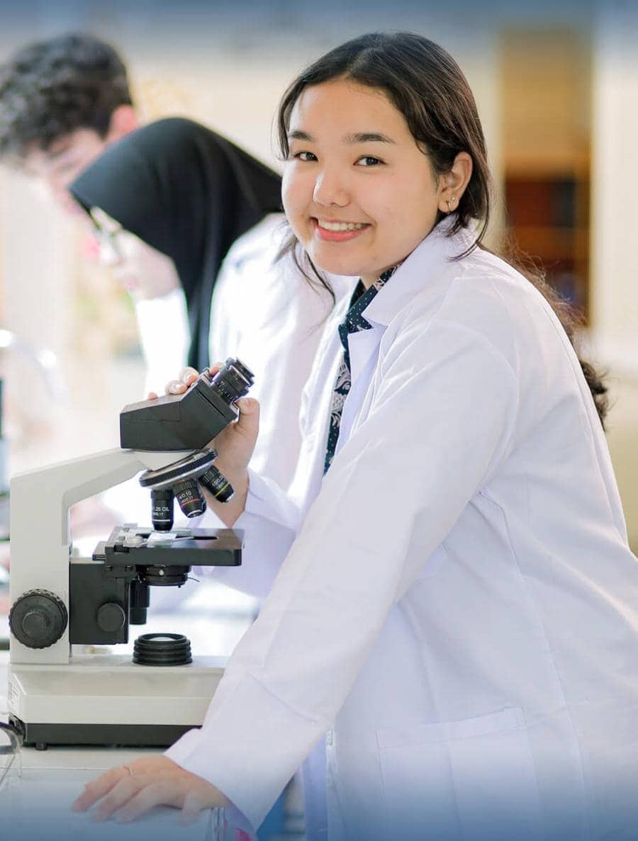 Young female student working with microscope in science lab at World Schools.