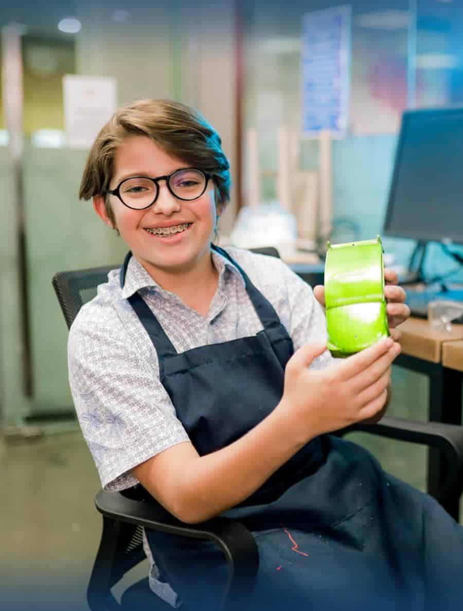 Innovative student in a classroom holding a green container, promoting creativity and modern education environments.