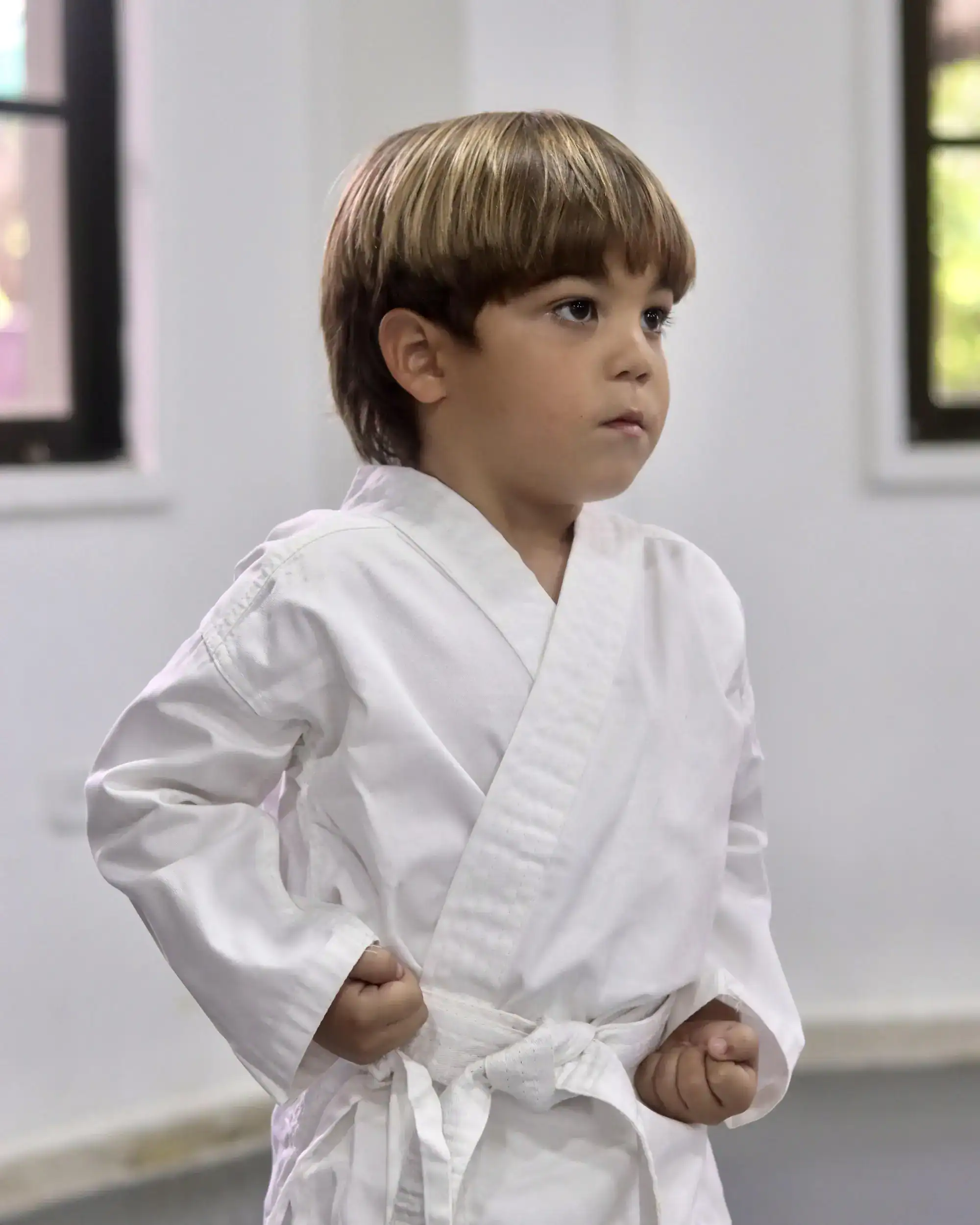 Bir dojo'da dövüş sanatları pratiği yapan genç çocuk, disiplin ve güven için beyaz bir gi giyiyor.