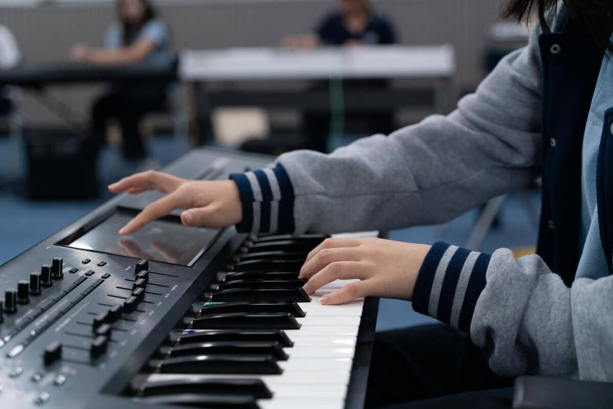Student playing digital keyboard at school music class for creative learning and development.