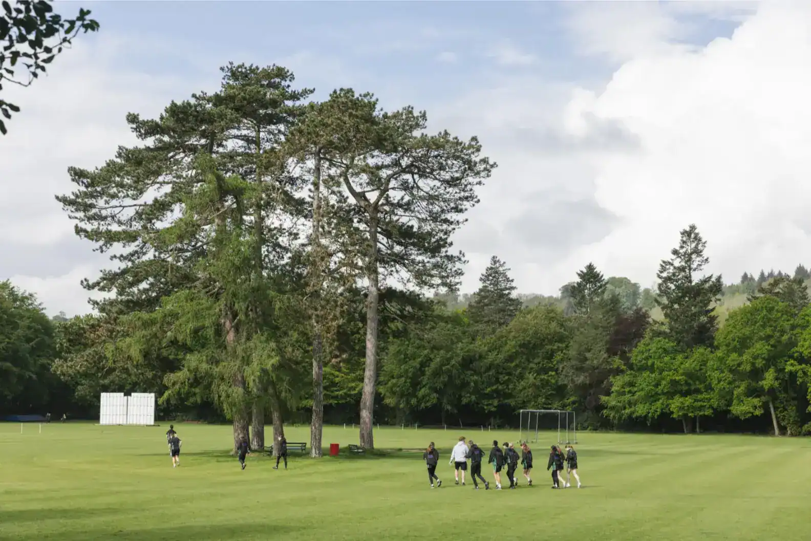 Students walking on lush green school field surrounded by tall trees, outdoor education, and nature exploration.
