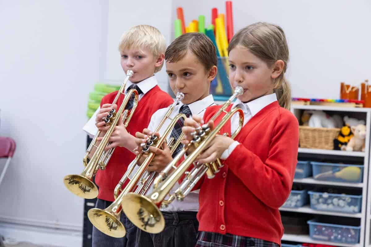 Young students practicing trumpet instruments in a classroom setting.