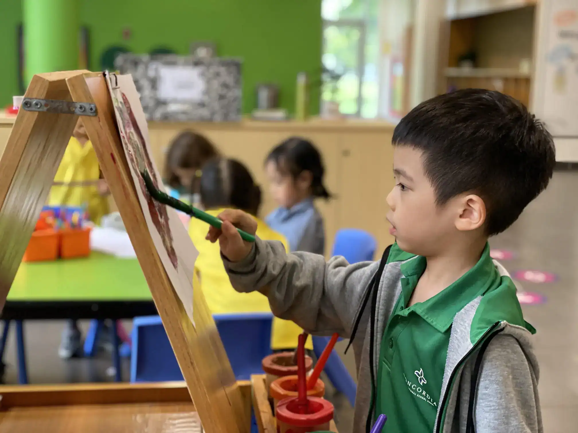 Bright young student painting colorful artwork in classroom with peers, fostering creativity and development.