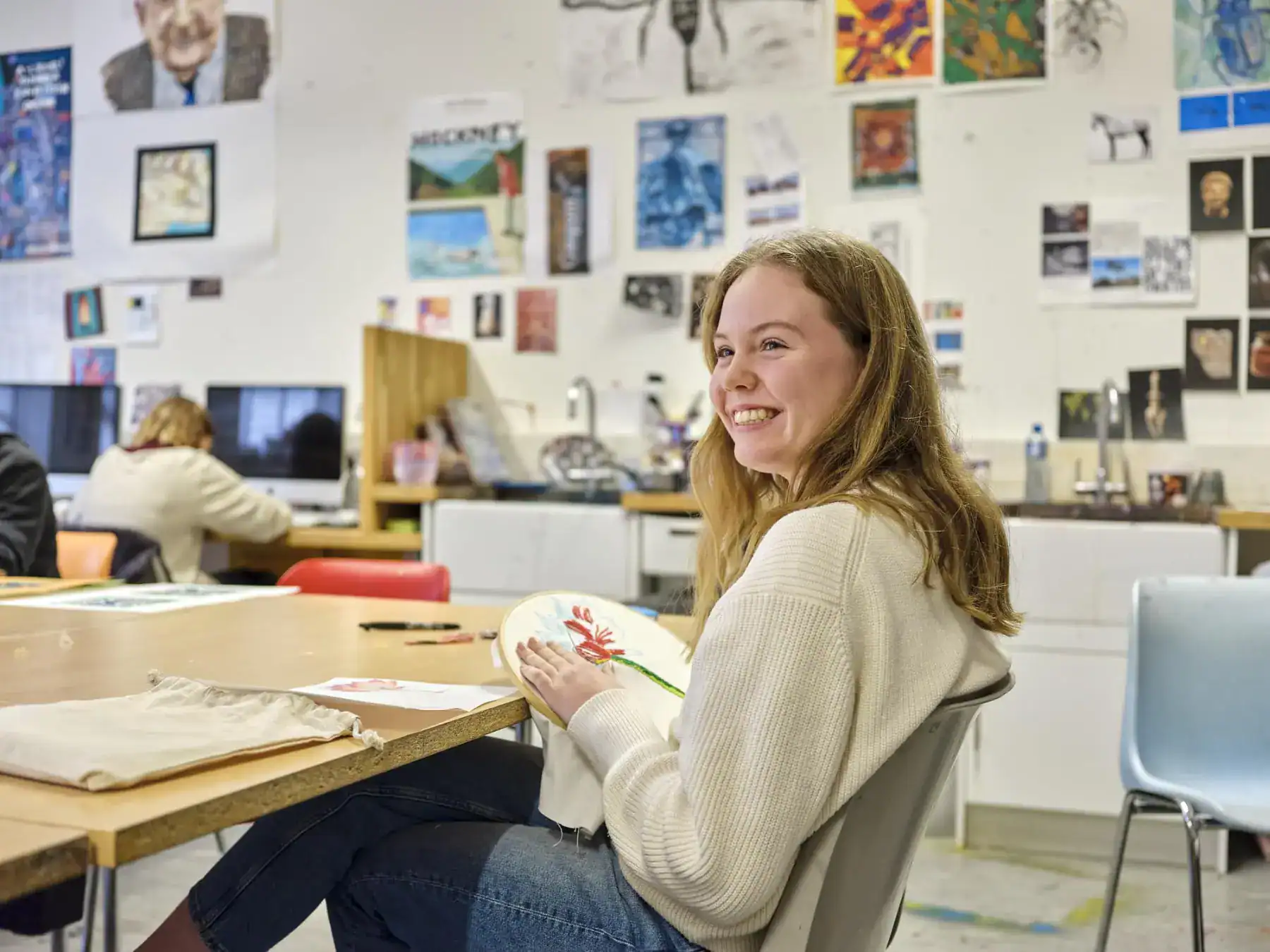 Bright young student smiling in art classroom with creative artwork displays on walls.