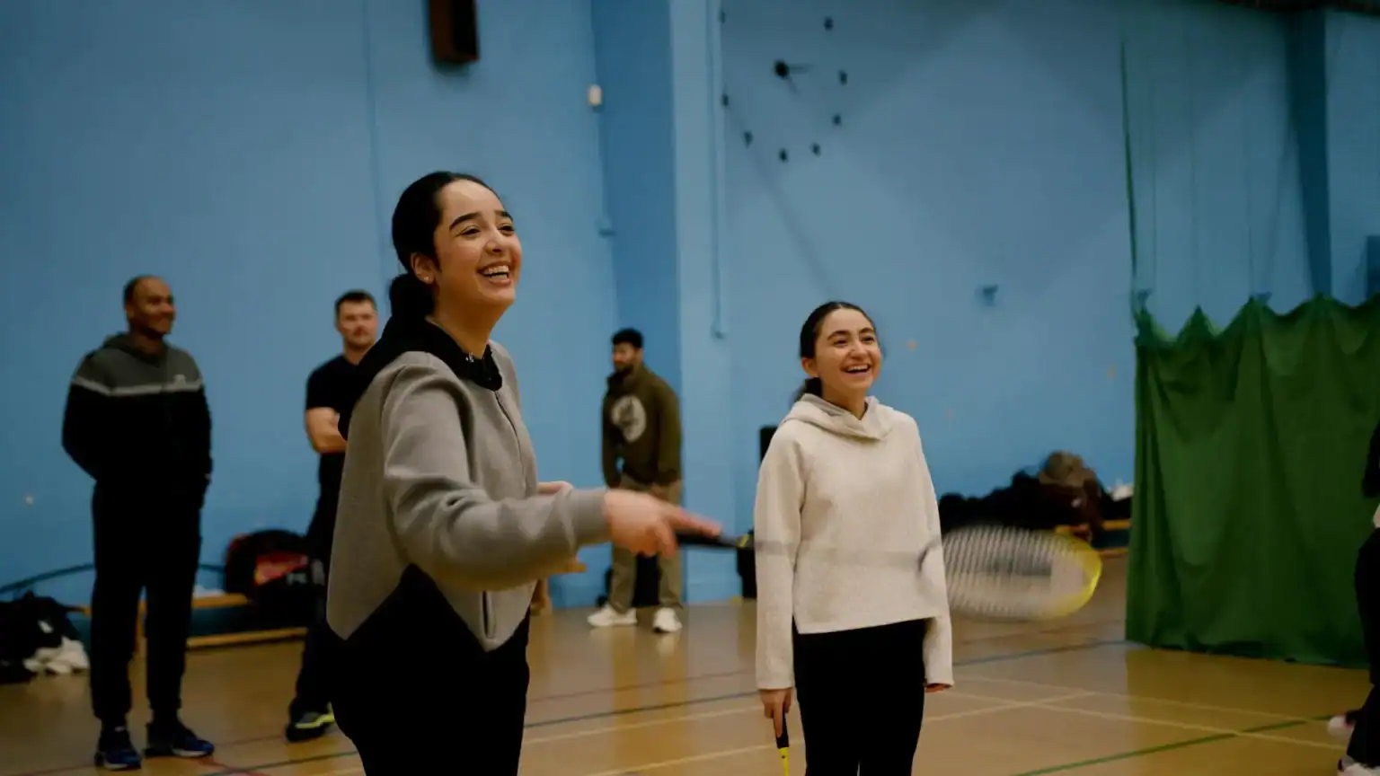 Happy students enjoying badminton class at a world school in a vibrant indoor gymnasium.