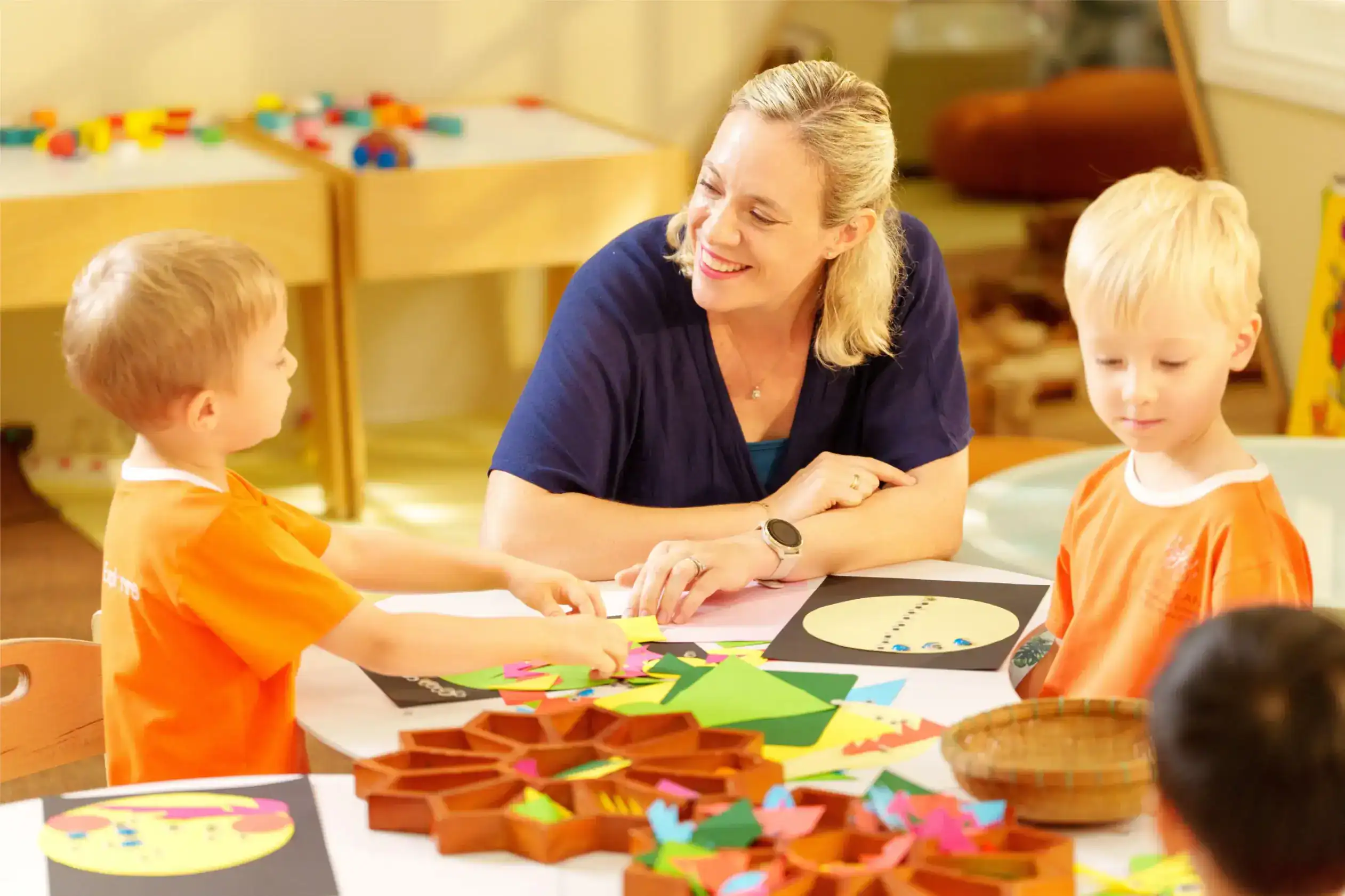 Creative preschool classroom with teacher and young children engaging in art activities at a table.