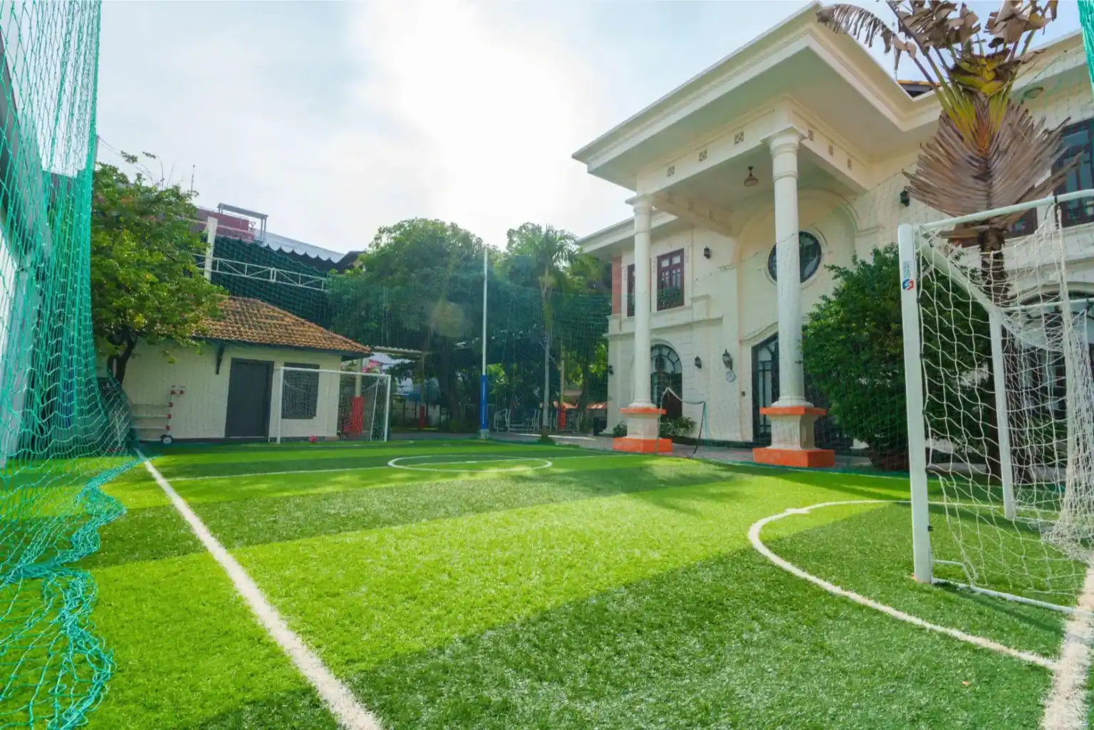 Lush green school sports field with soccer goal and residential building in background.