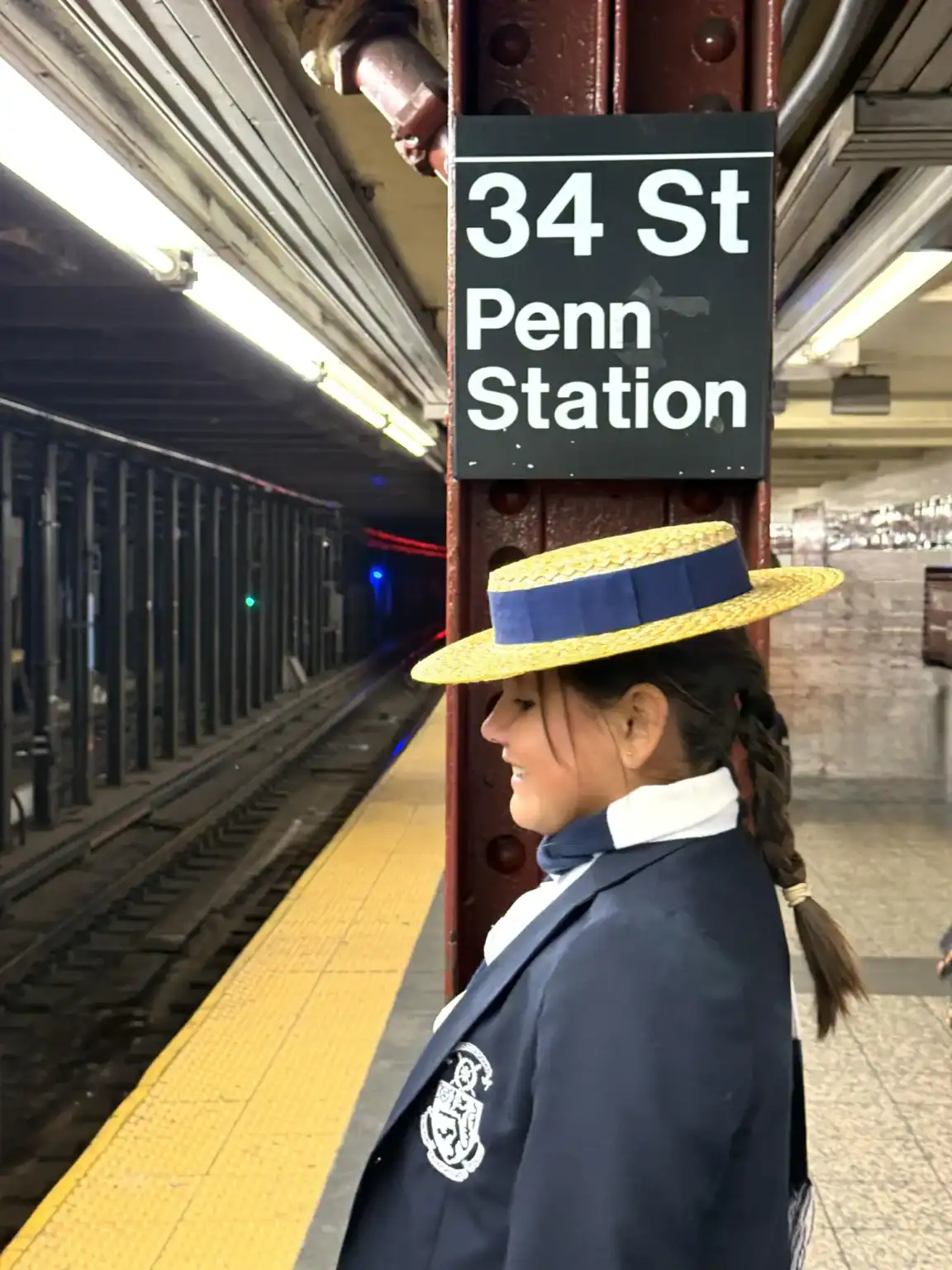 Girl in school uniform with straw hat at Penn Station subway platform.