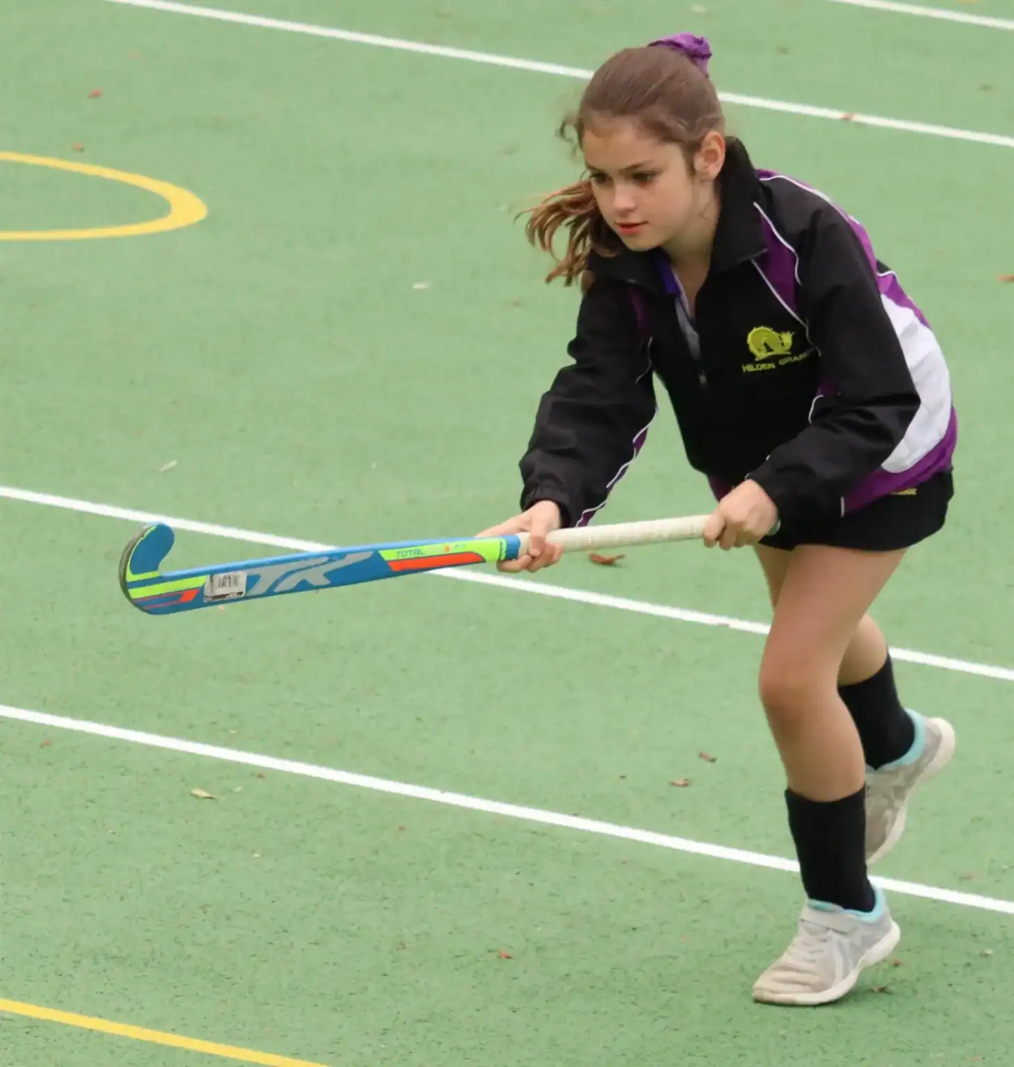 Active young girl playing field hockey on school sports court for sport and fitness development.