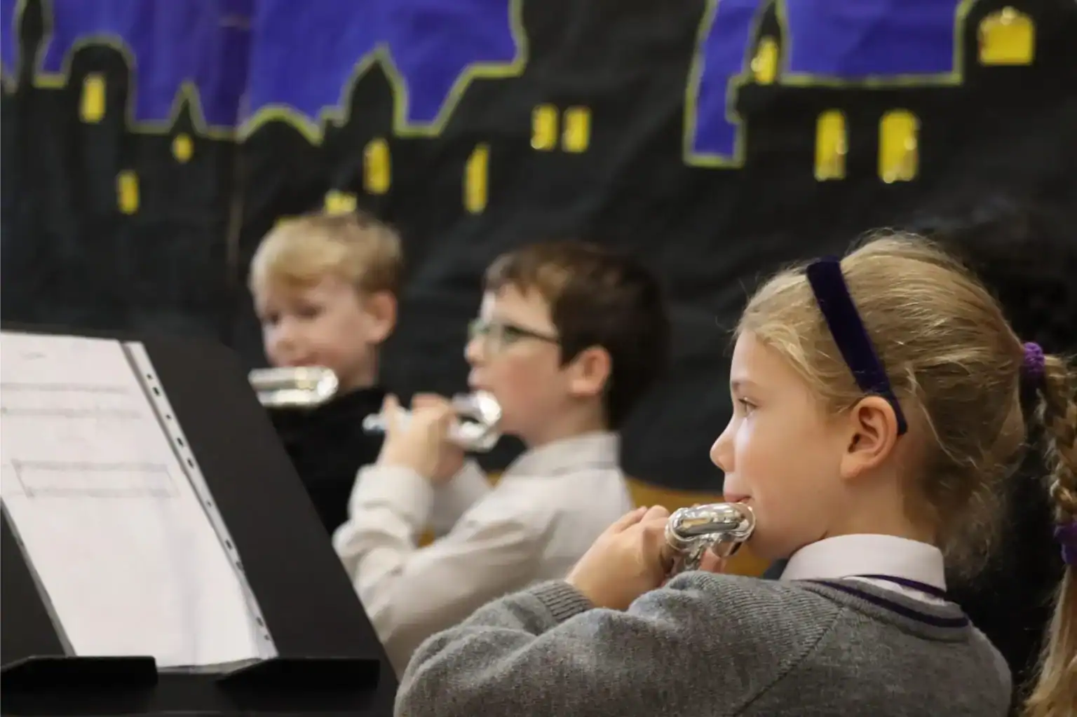 Focused children playing flutes during school music class at an international school event.