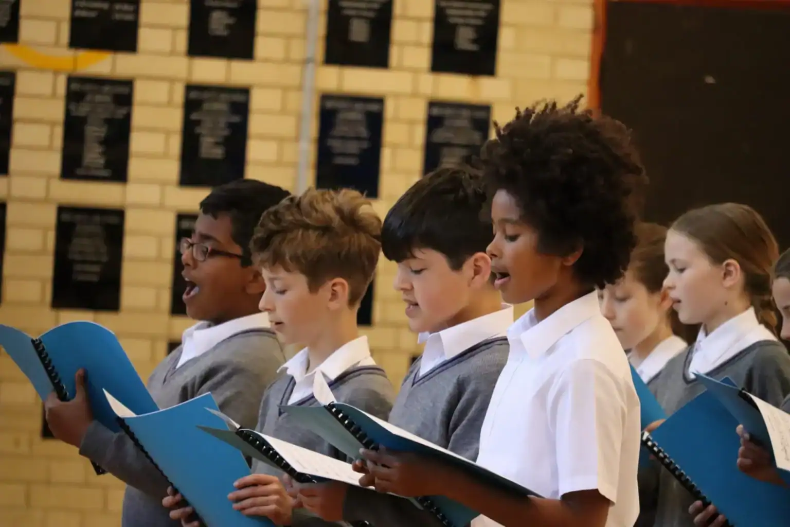 Diverse students singing choir with blue songbooks in a classroom or school hall.