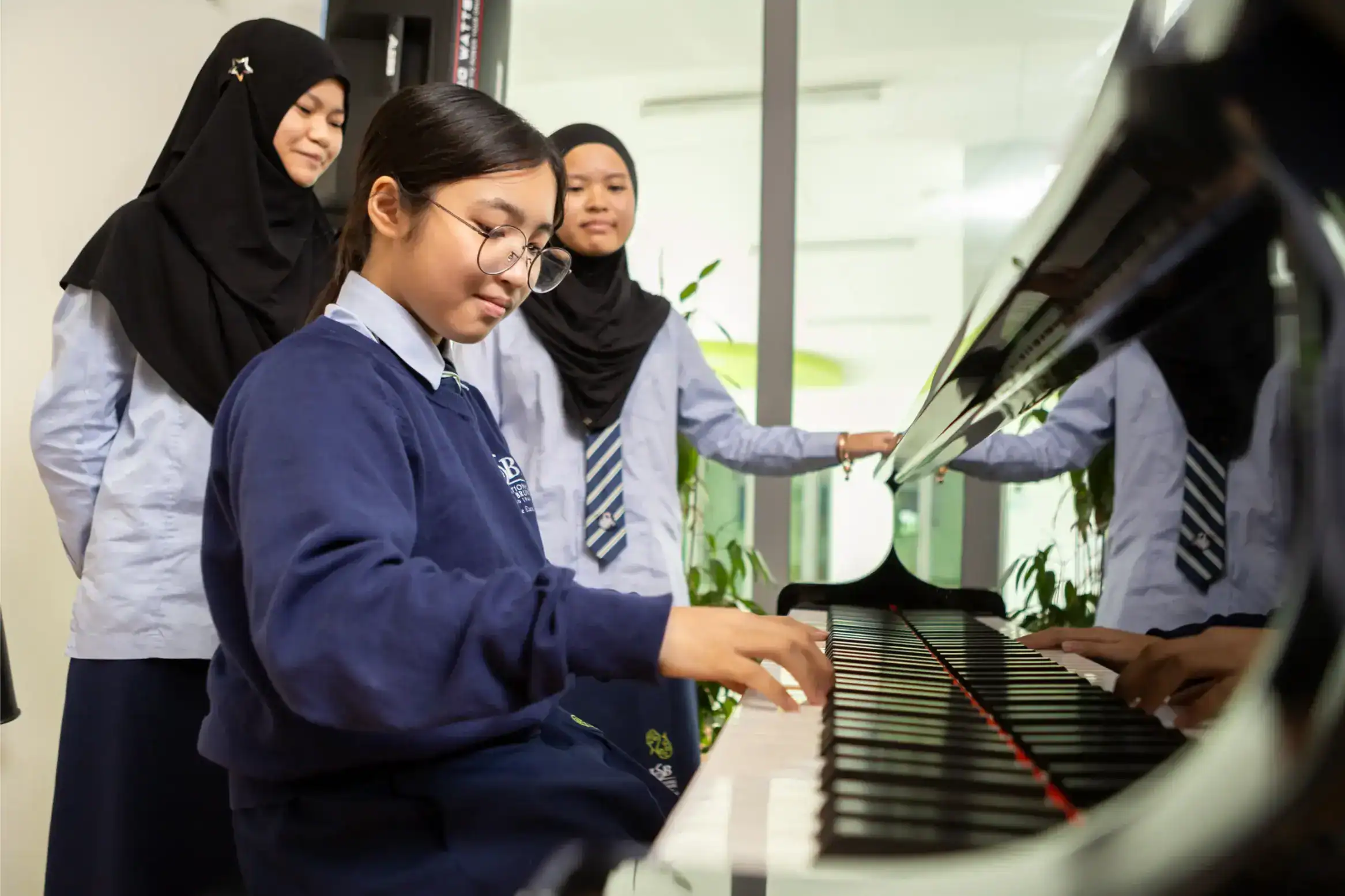 Focused Asian girl playing piano with three classmates observing, in a modern school setting.