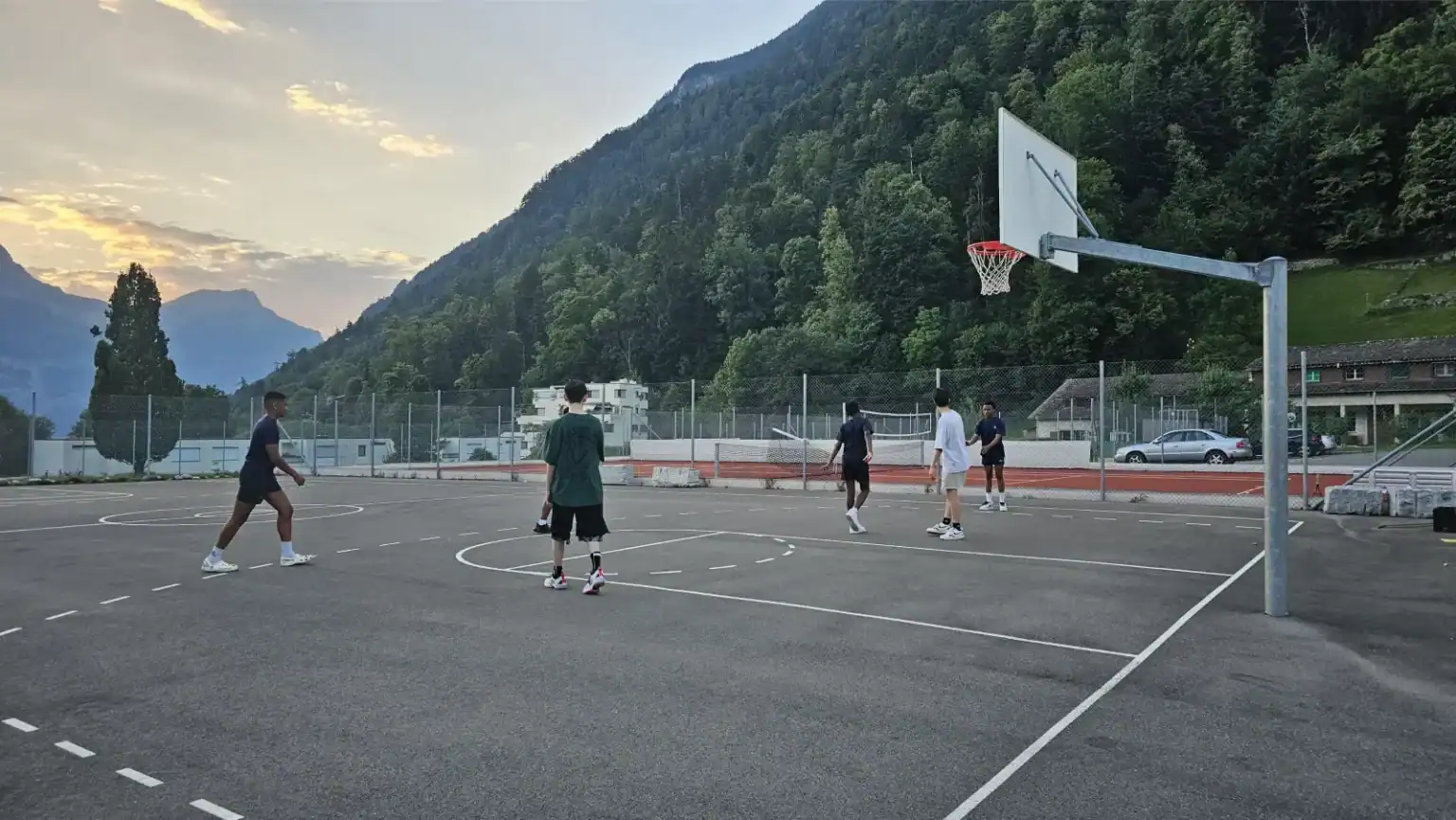 Students playing basketball on an outdoor court in a scenic mountain setting.