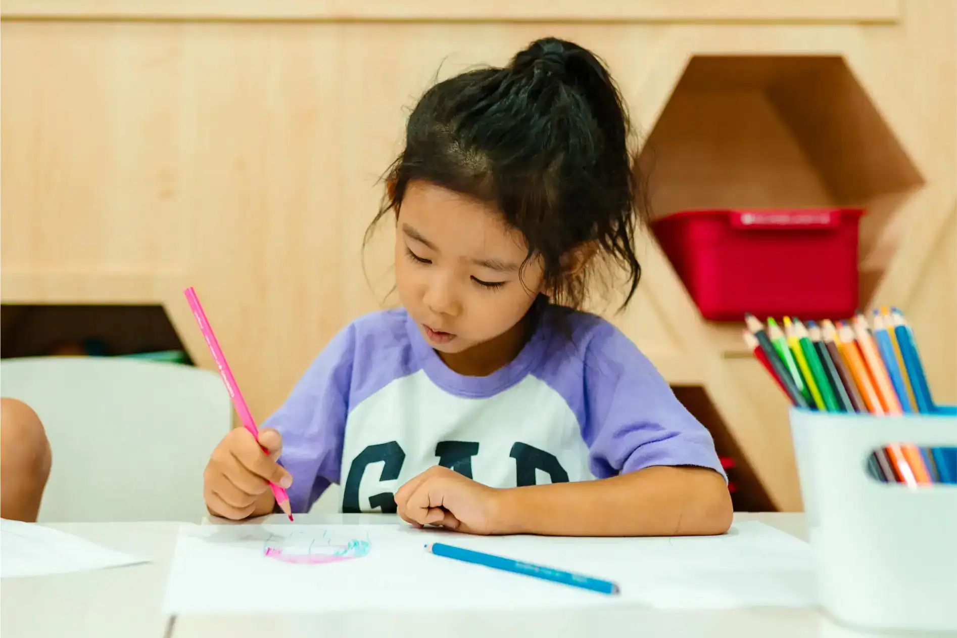 Colorida joven dibujando con rotuladores en una mesa en un aula creativa.