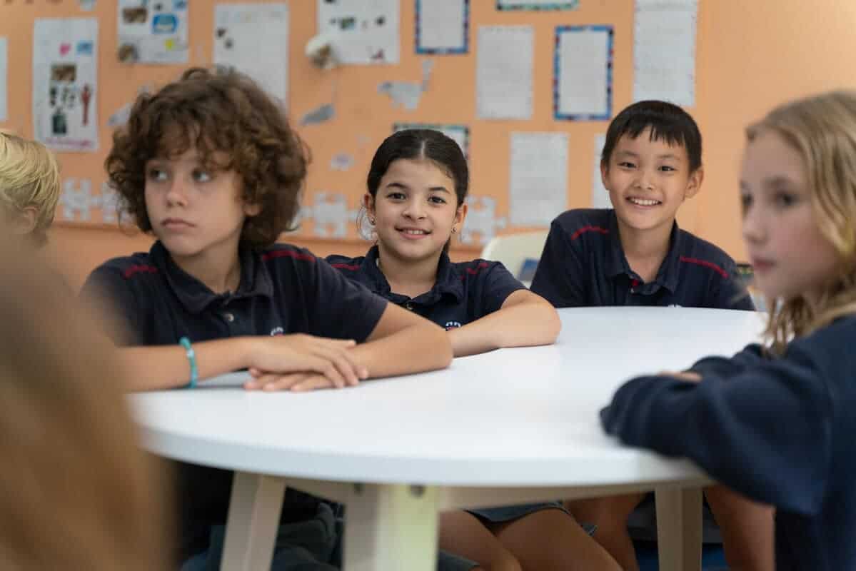 Young diverse students sitting at a classroom table, engaged in learning at a World Schools education center.
