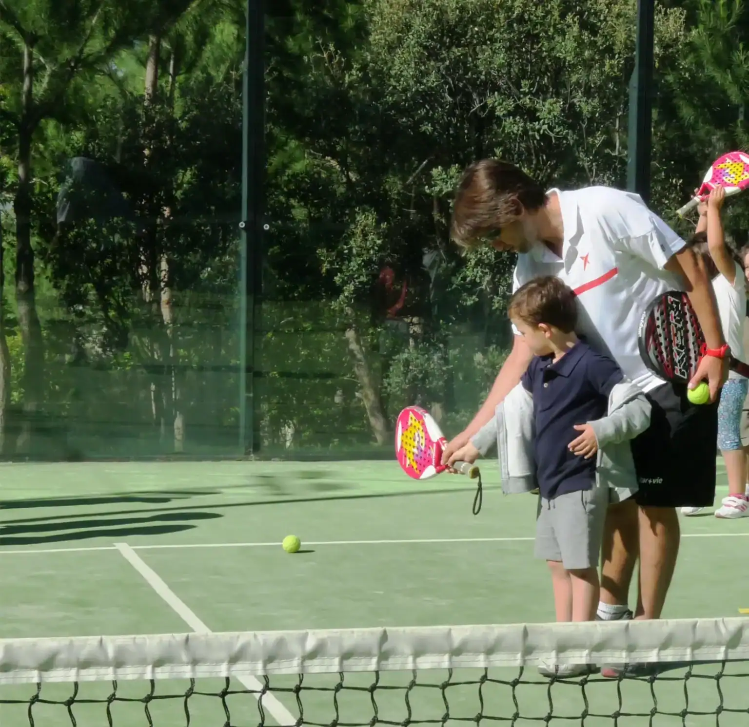 Young boy with a tennis paddle on a court, guided by an instructor during tennis lesson.