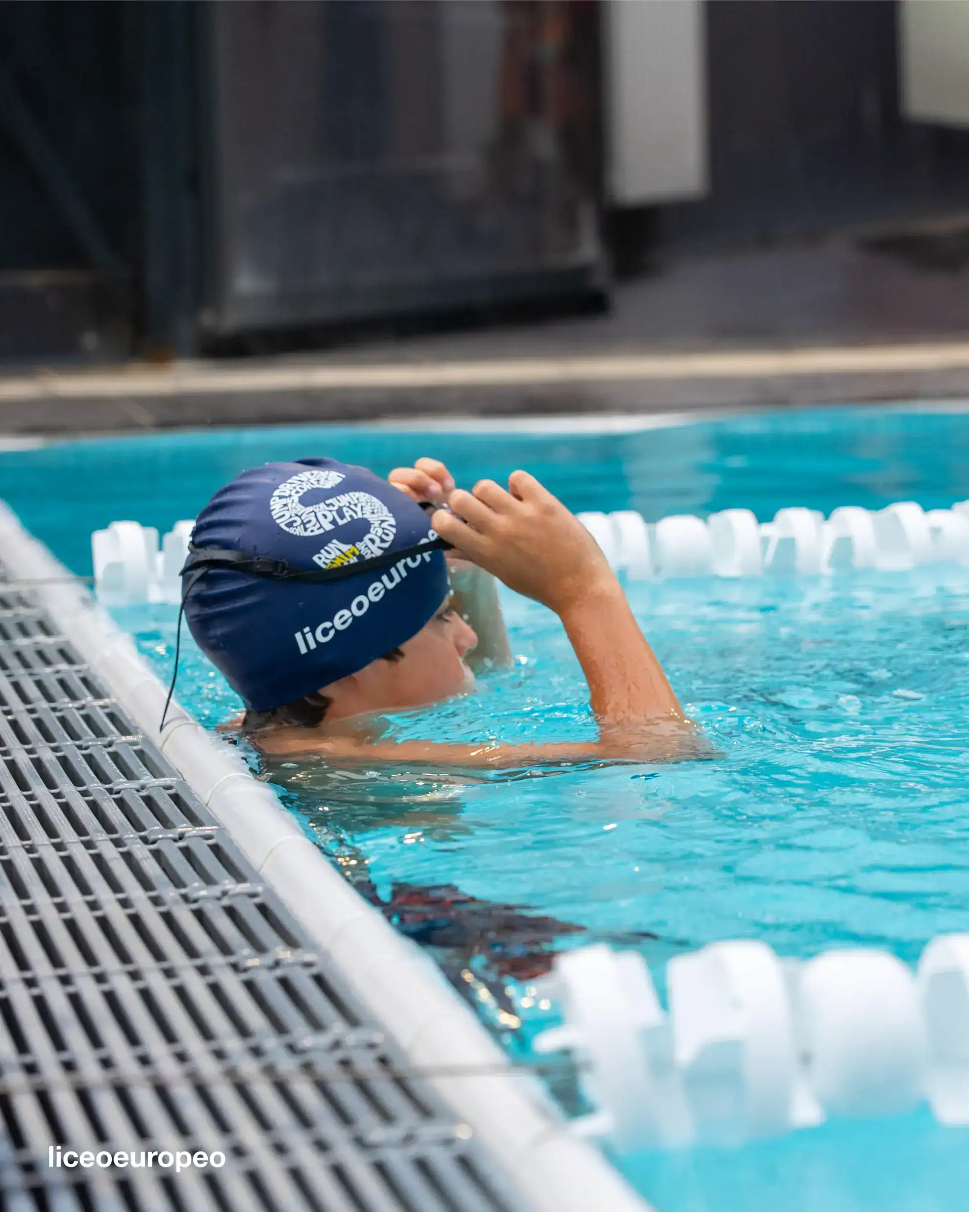 Young swimmer adjusting swim cap at school swimming pool in a competitive sports setting.