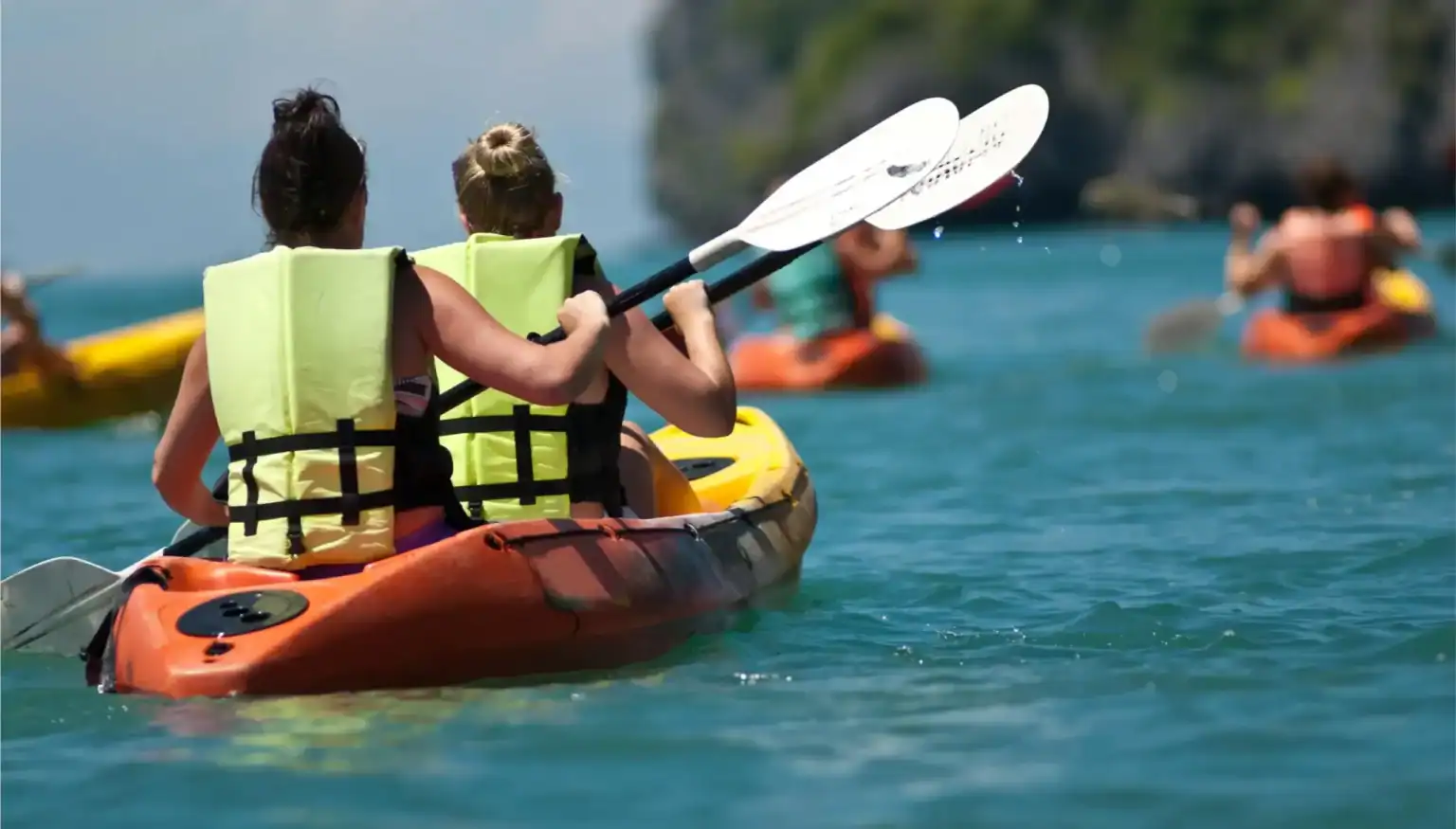Children kayaking on a clear blue lake during outdoor educational activities at an international school.