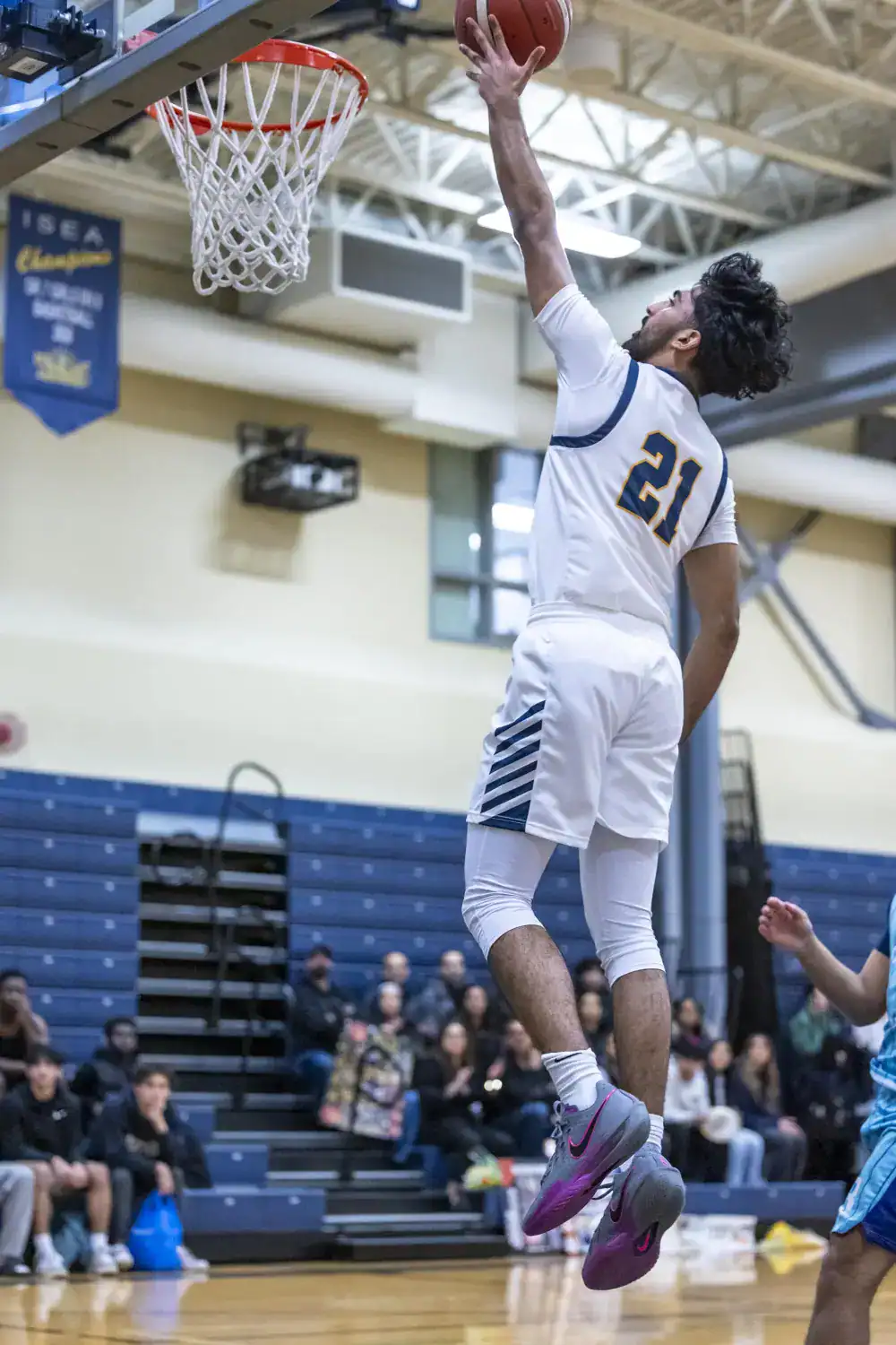 Athlete jumping for basketball shot in indoor gym at a school sports event.
