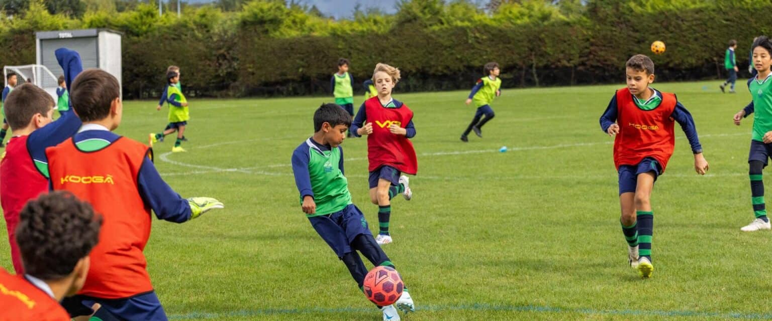 Young children playing soccer on a lush green field at an international school sports day.