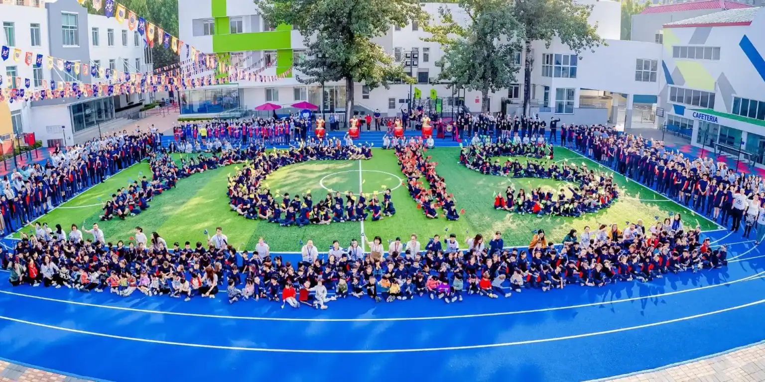Children forming "WORLD SCHOOLS" on school sports field with students, teachers, and colorful decorations in the background.