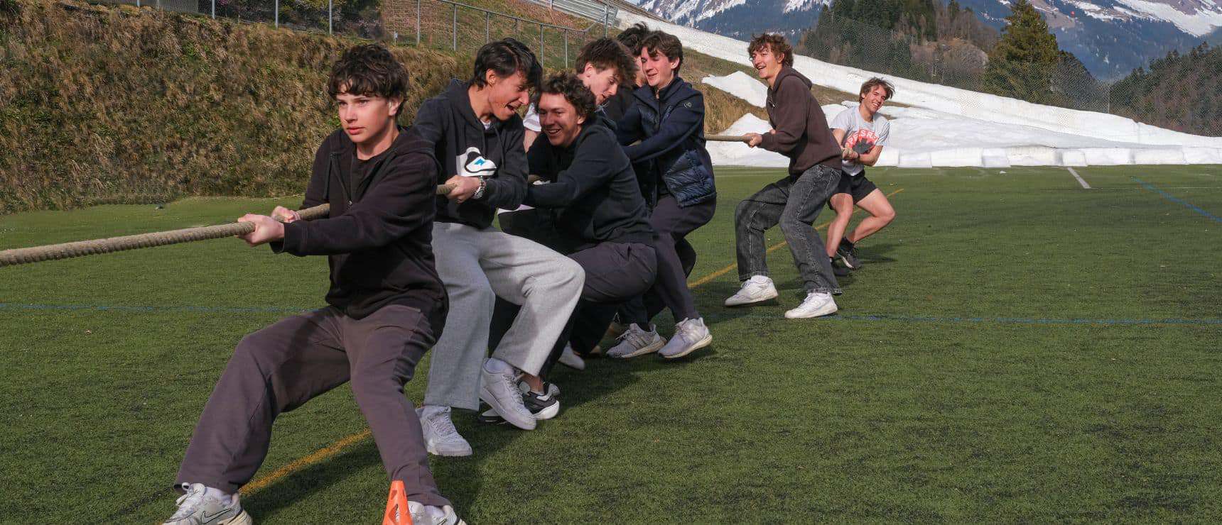 Youth tug-of-war game on school field with mountains in background; outdoor sports at world schools.