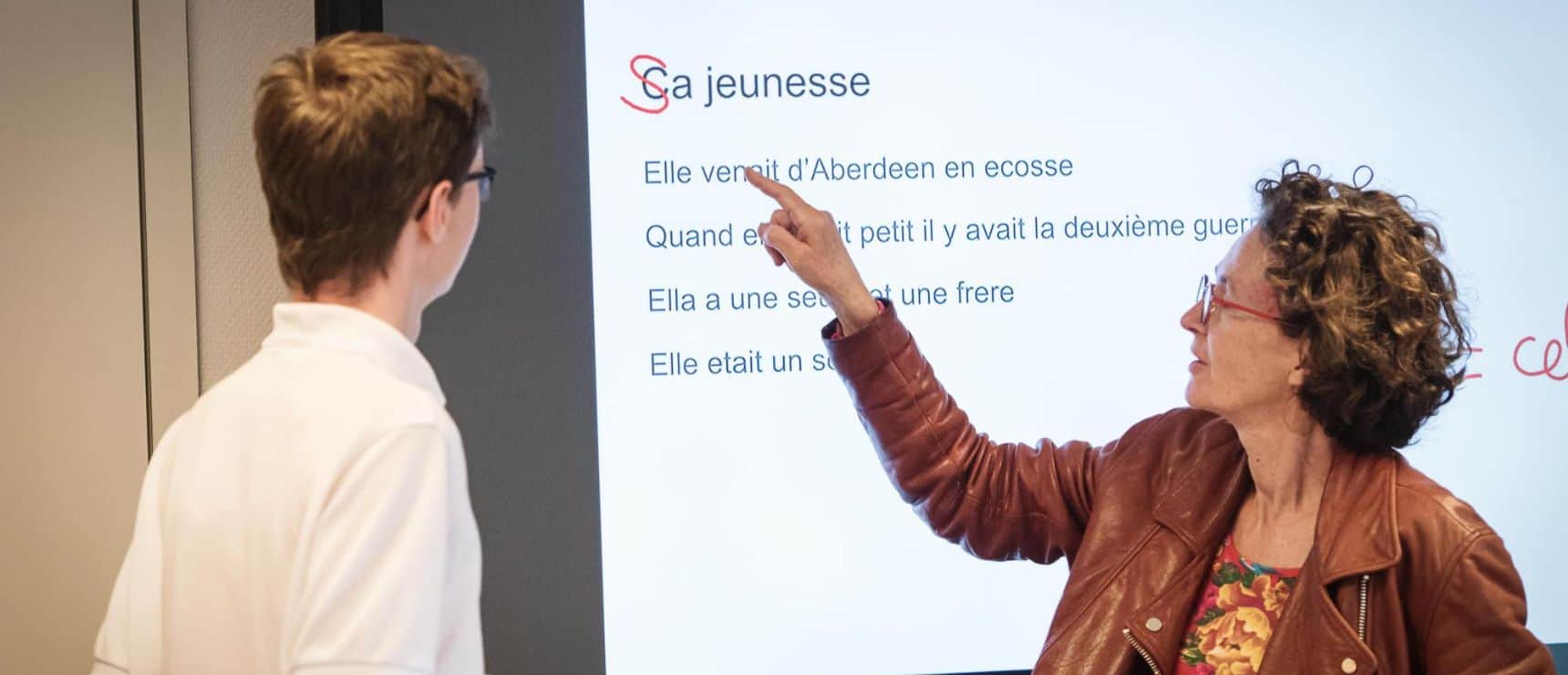 High school teacher explaining French lesson to student in classroom, focusing on language learning and education.