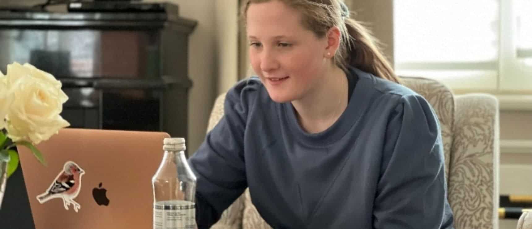 Bright girl studying online with laptop and water bottle at home for global education excellence.