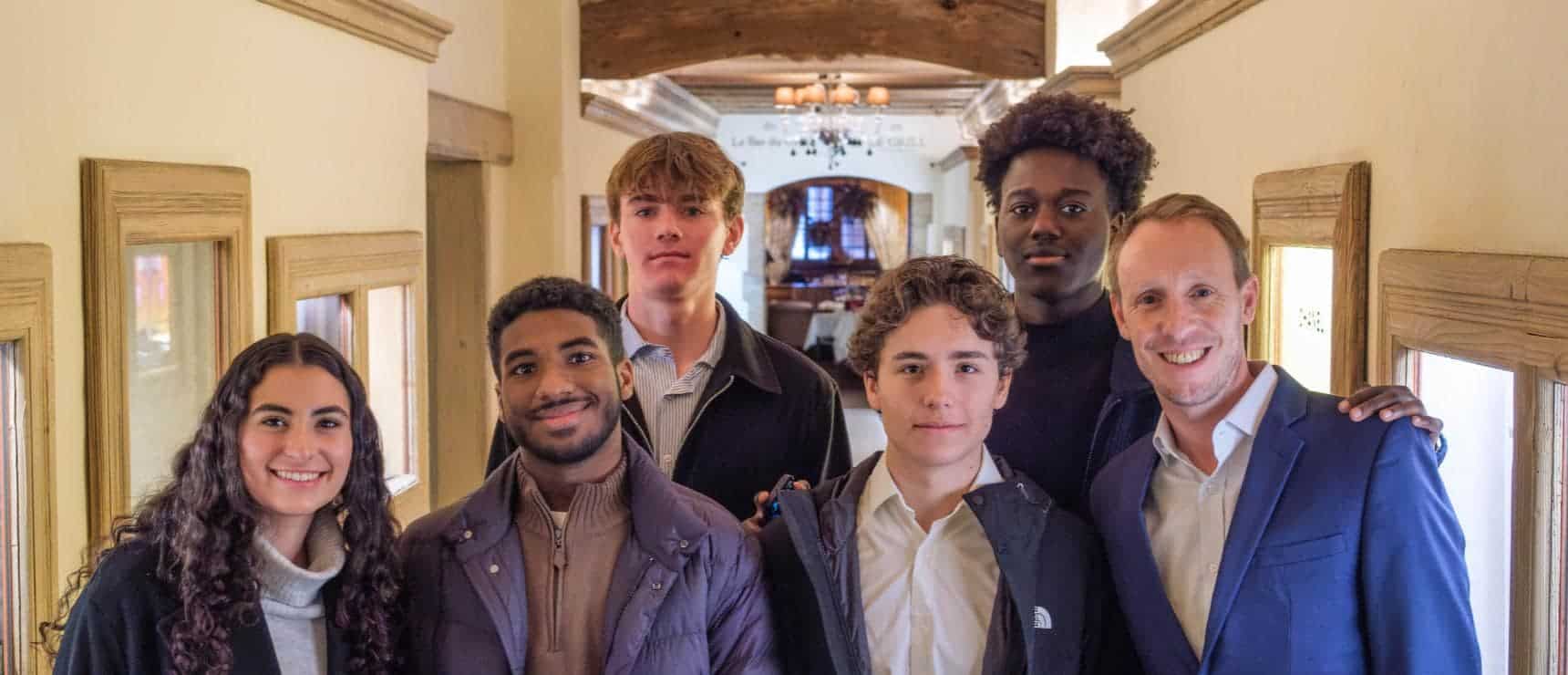 Diverse group of students and teacher smiling inside a school hallway, promoting international education.