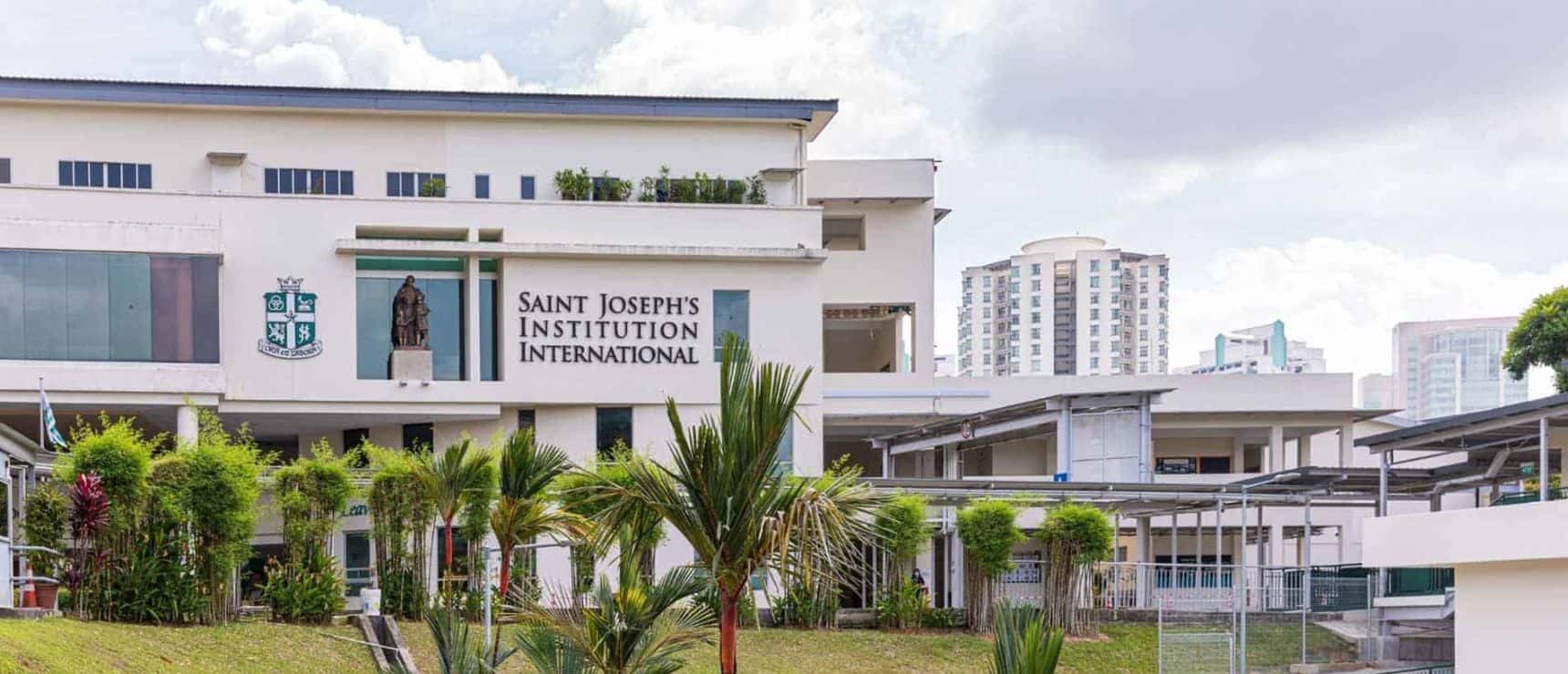 School building exterior with Saint Joseph's Institution International signage in a lush green setting.