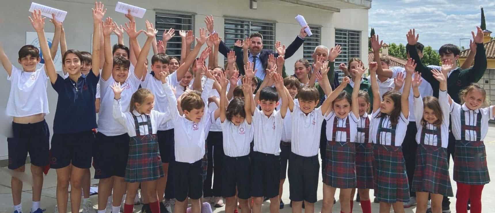 Engaged young students celebrating outdoors at school, smiling and raising hands for community spirit.