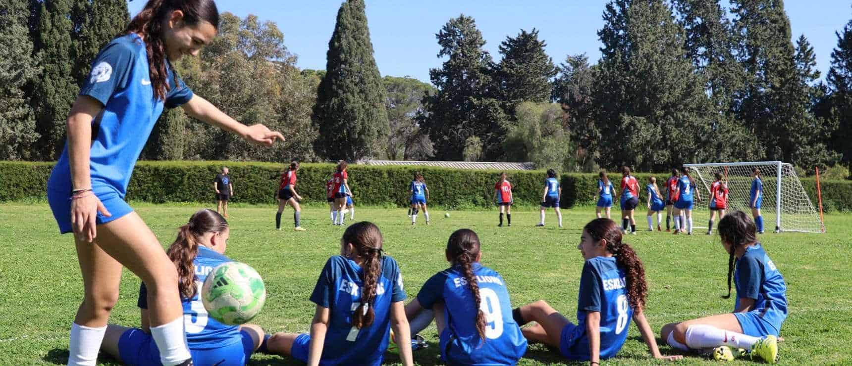 Soccer girls team resting during outdoor match at school sports field.