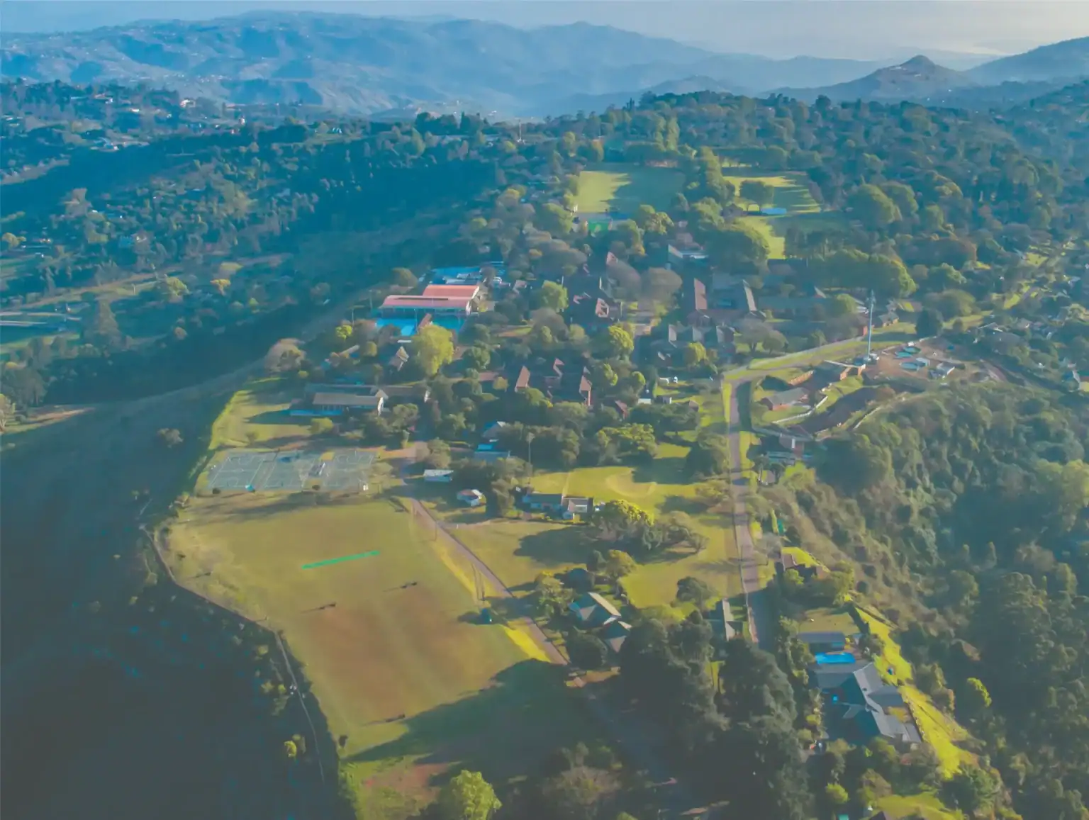 Aerial view of a lush, green international school campus surrounded by nature and mountains.