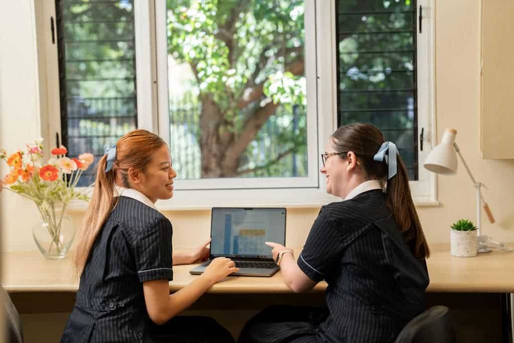 Two students studying together at a school desk with a laptop.