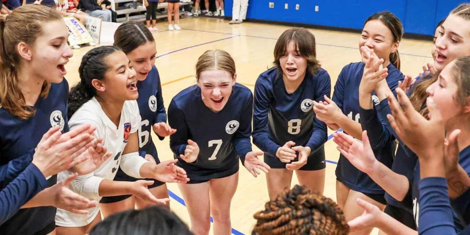 Energetic girls volleyball team celebrating victory in school gym.