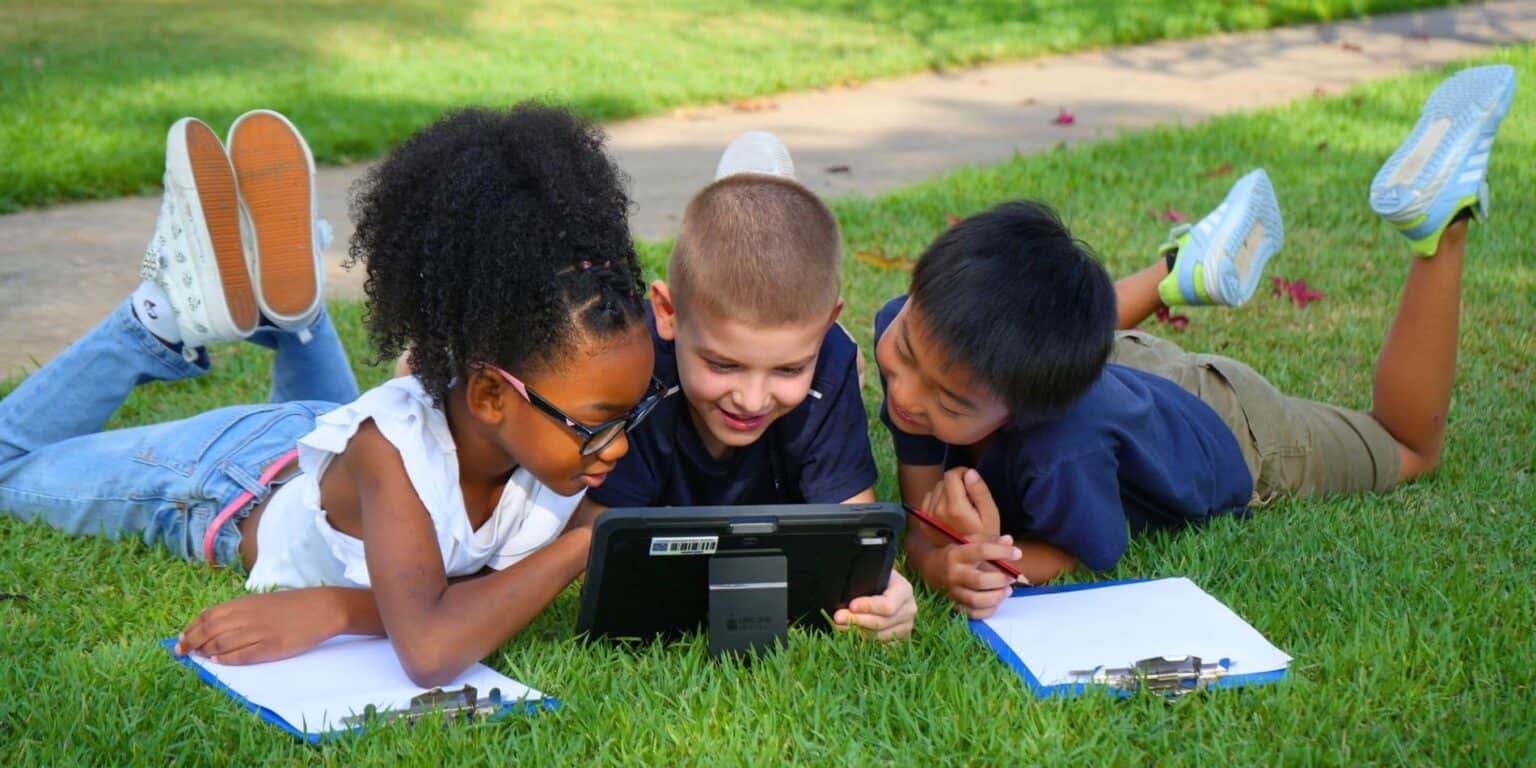 أطفال مستلقون على العشب، متفاعلون مع الجهاز اللوحي، في الهواء الطلق، متنوعون، يتعلمون، مرحون، مستعدون للمستقبل، تعليم، أنشطة في الهواء الطلق، أطفال سعداء.