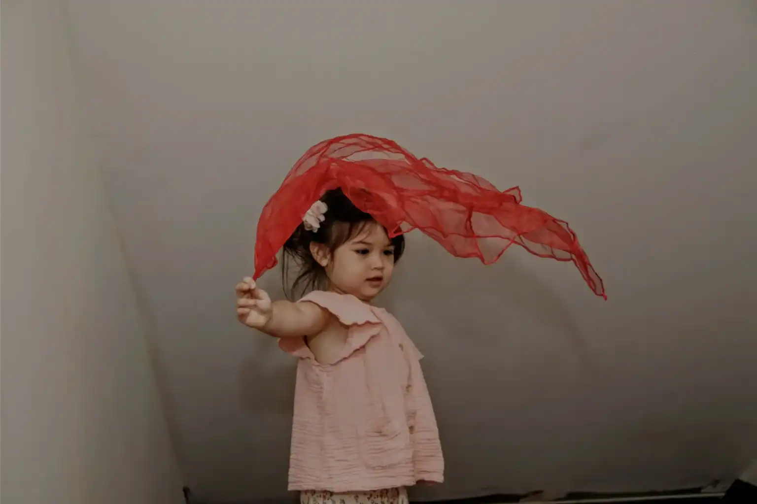 Colorful young girl playing with red fabric, enjoying creative learning in a preschool setting.