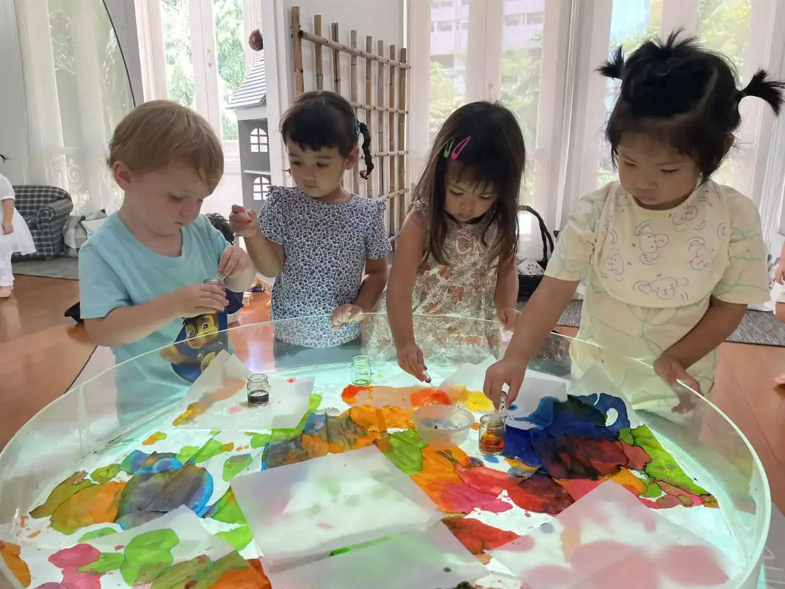 Painted children engaging in creative art activity at a glass table.