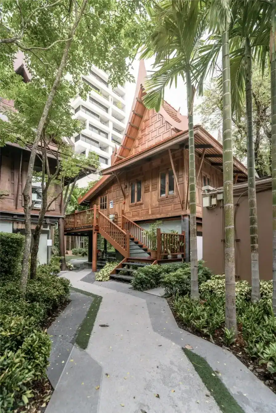 Traditional Thai-style wooden school building surrounded by lush greenery and tall trees.