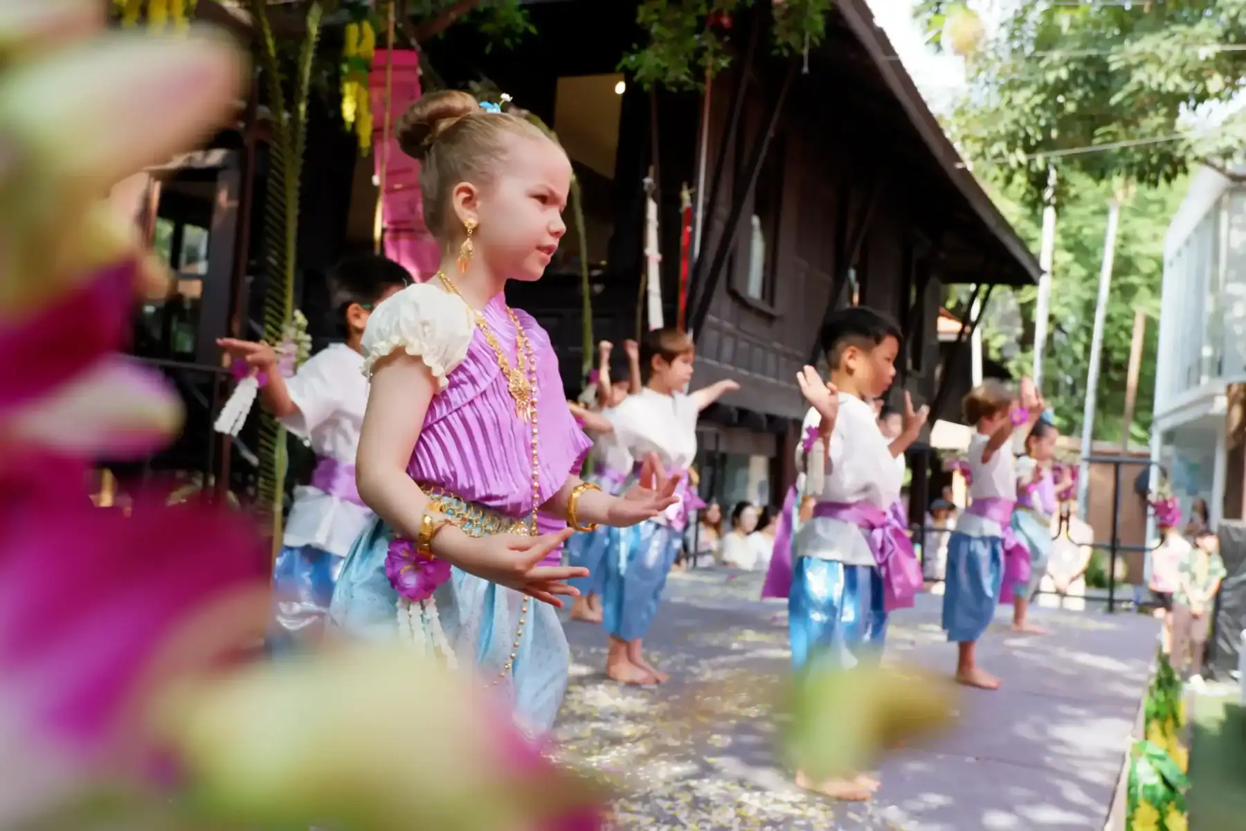 A girl in traditional Thai costume performing a dance outdoors.