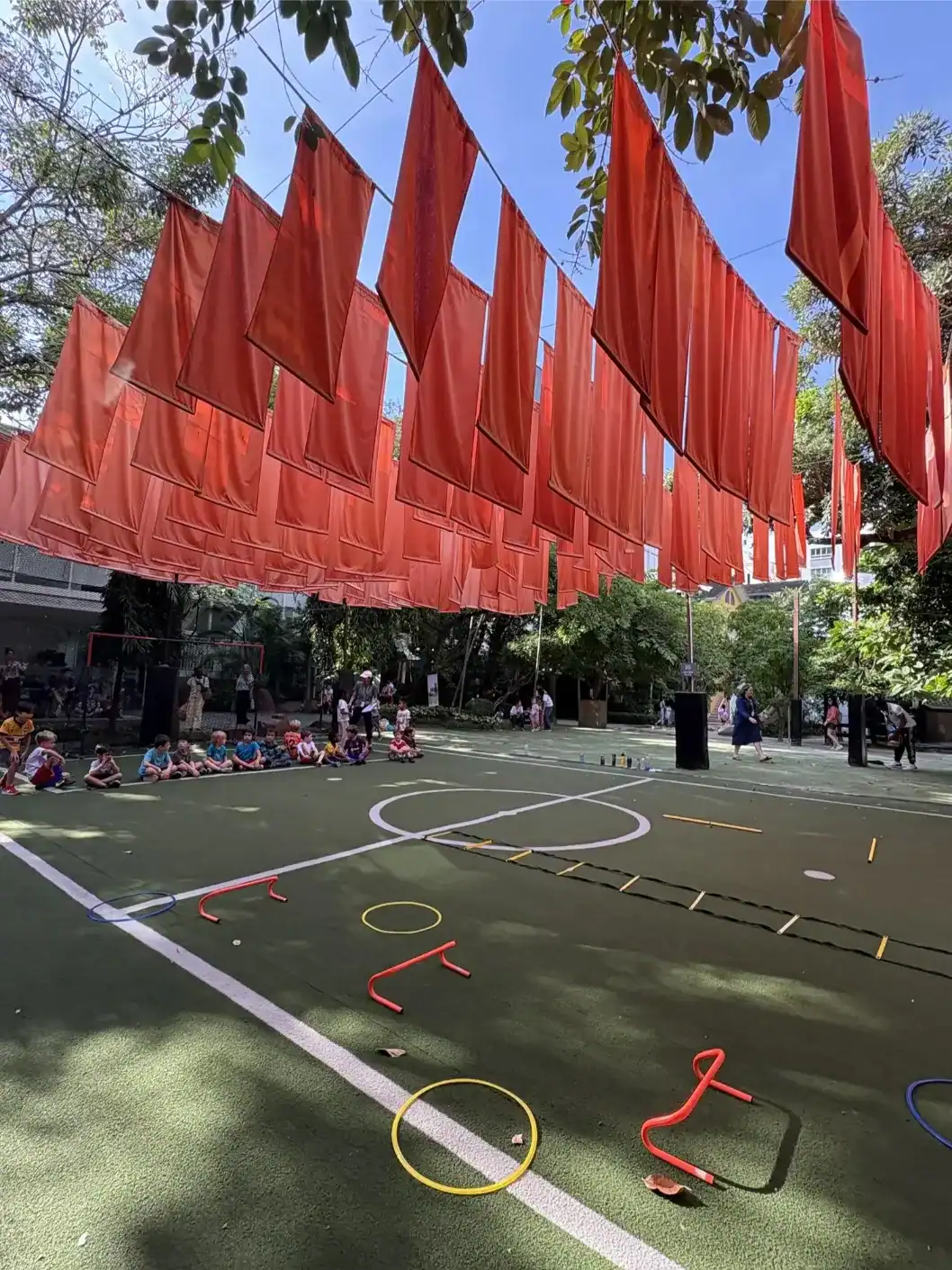 Red flags hanging above a school playground with children sitting on the ground and outdoor sports e.