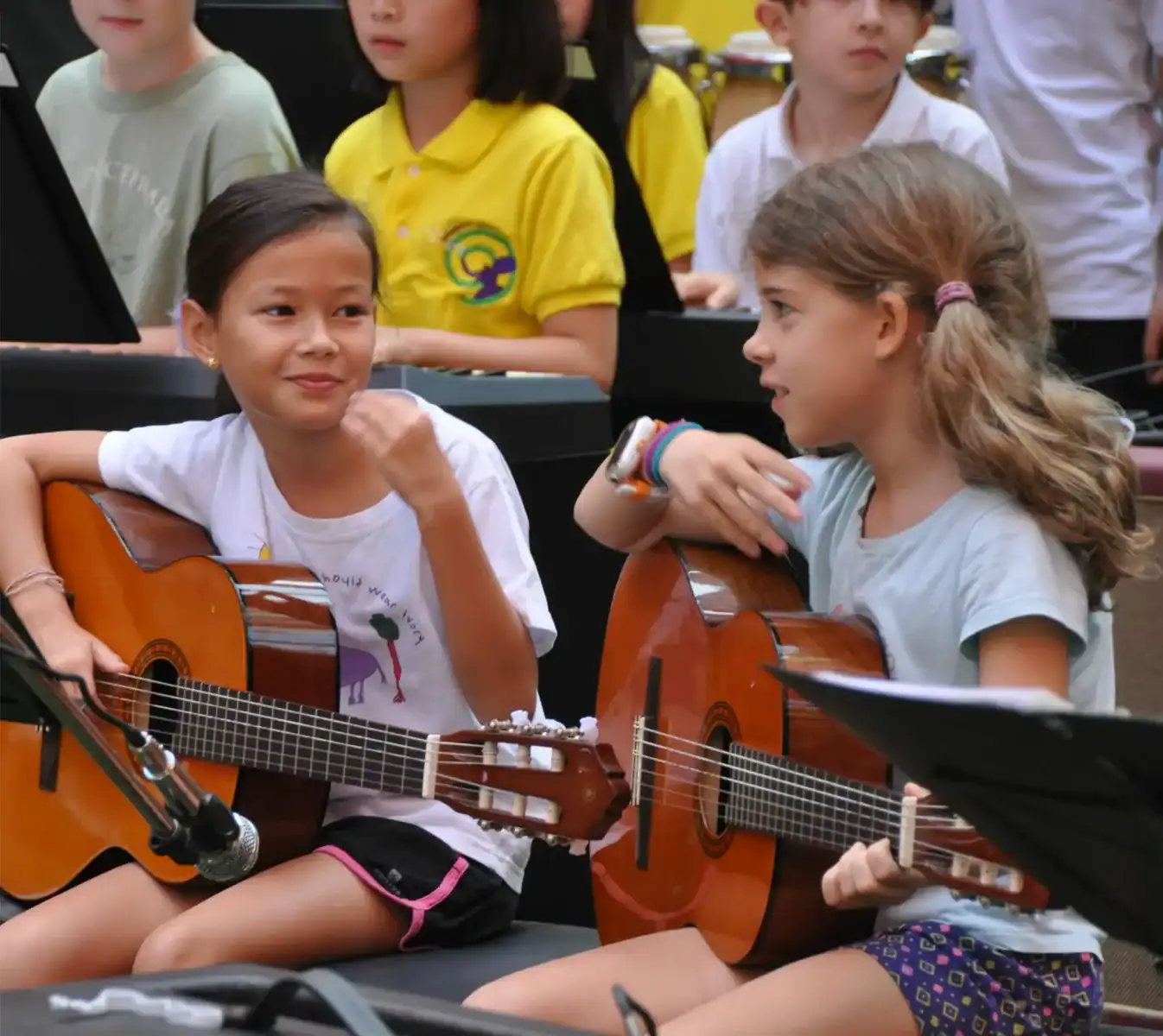 Young girls playing acoustic guitars during a music class at an international school event.