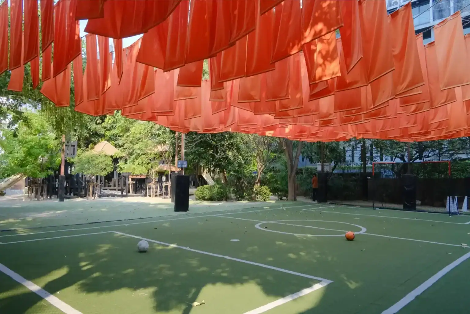Outdoor sports court with hanging orange fabric shades and trees in the background.