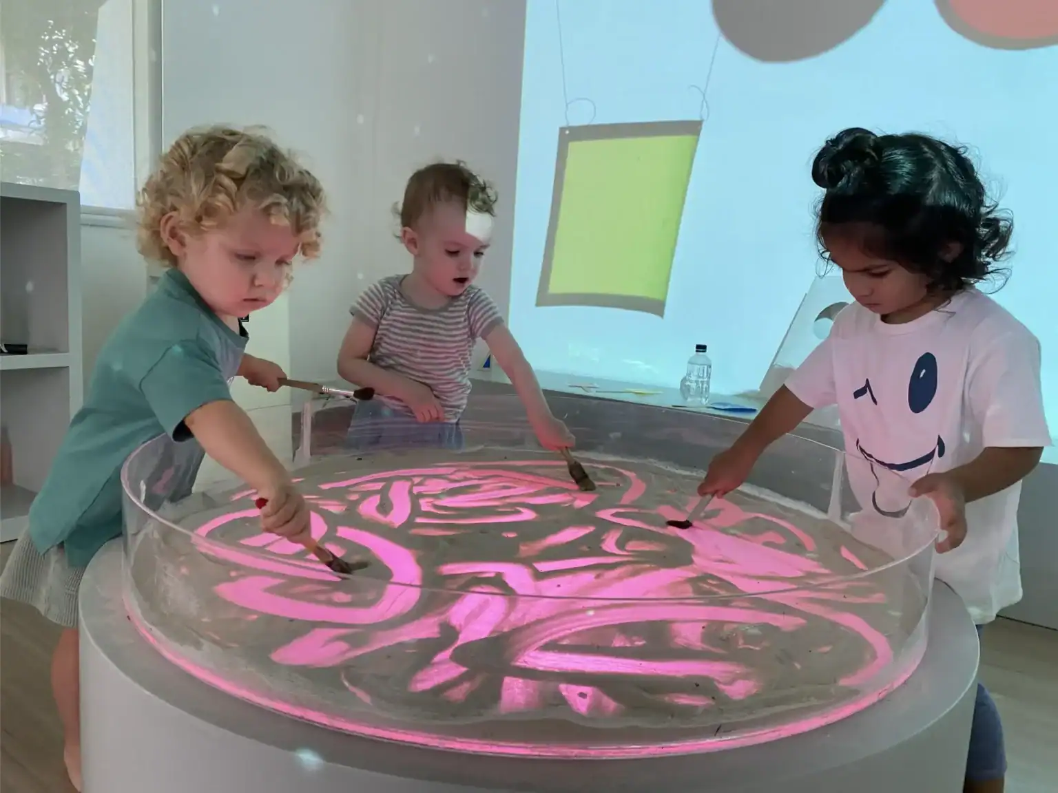 Children engaging with an interactive light-up sand table in a modern classroom.