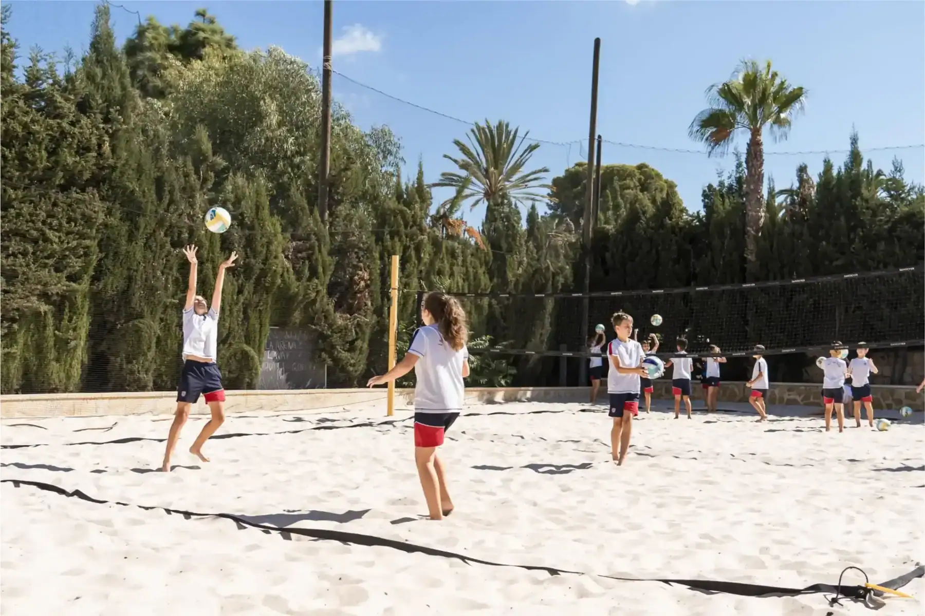 Kids playing beach volleyball outdoors at a global school.