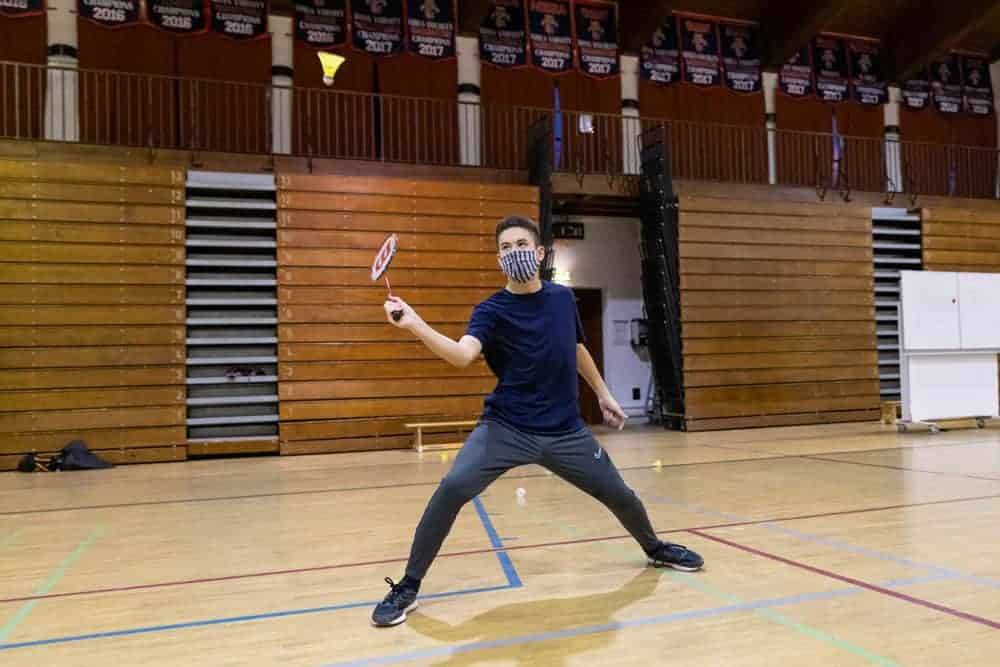 Flexible student playing badminton indoors at a World Schools event, showcasing athletic talent and focus.