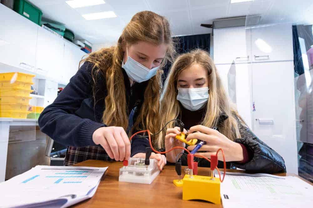Innovative learning in world schools, students engaged in science experiment with electrical circuit testing.