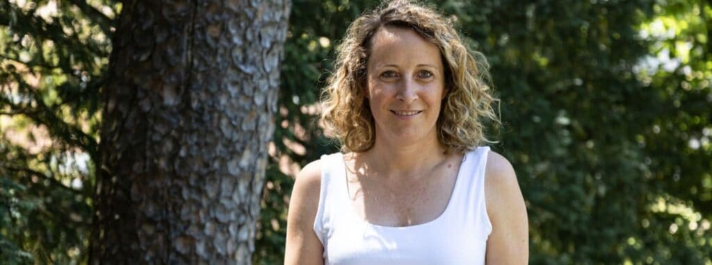 Learning outdoors at a world school with a smiling woman surrounded by trees and nature.