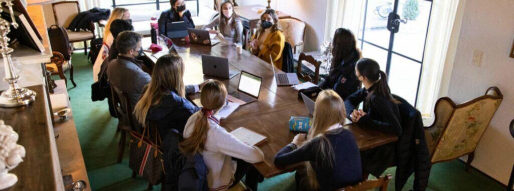 Students attending a global school meeting with laptops and notebooks for international education.