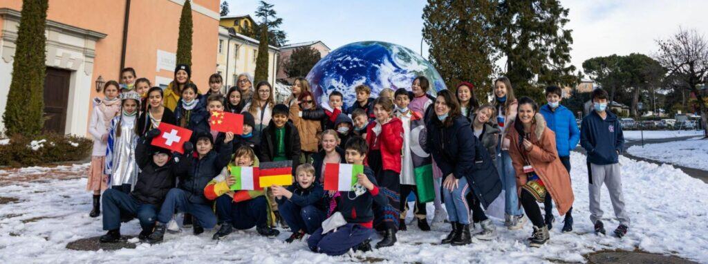 Students of diverse nationalities holding flags in front of a large globe at a World Schools event.
